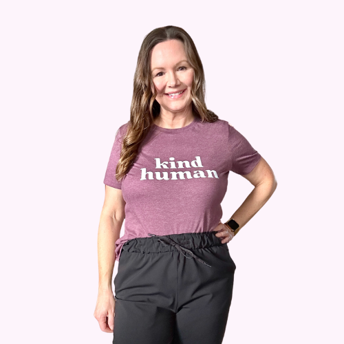 Woman smiling wearing a Mauve 'Kind Human' T-shirt paired with black pants.
