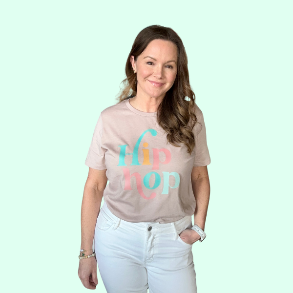 Woman smiling in a beige t-shirt with a colorful 'Hip Hop' text design, paired with white pants