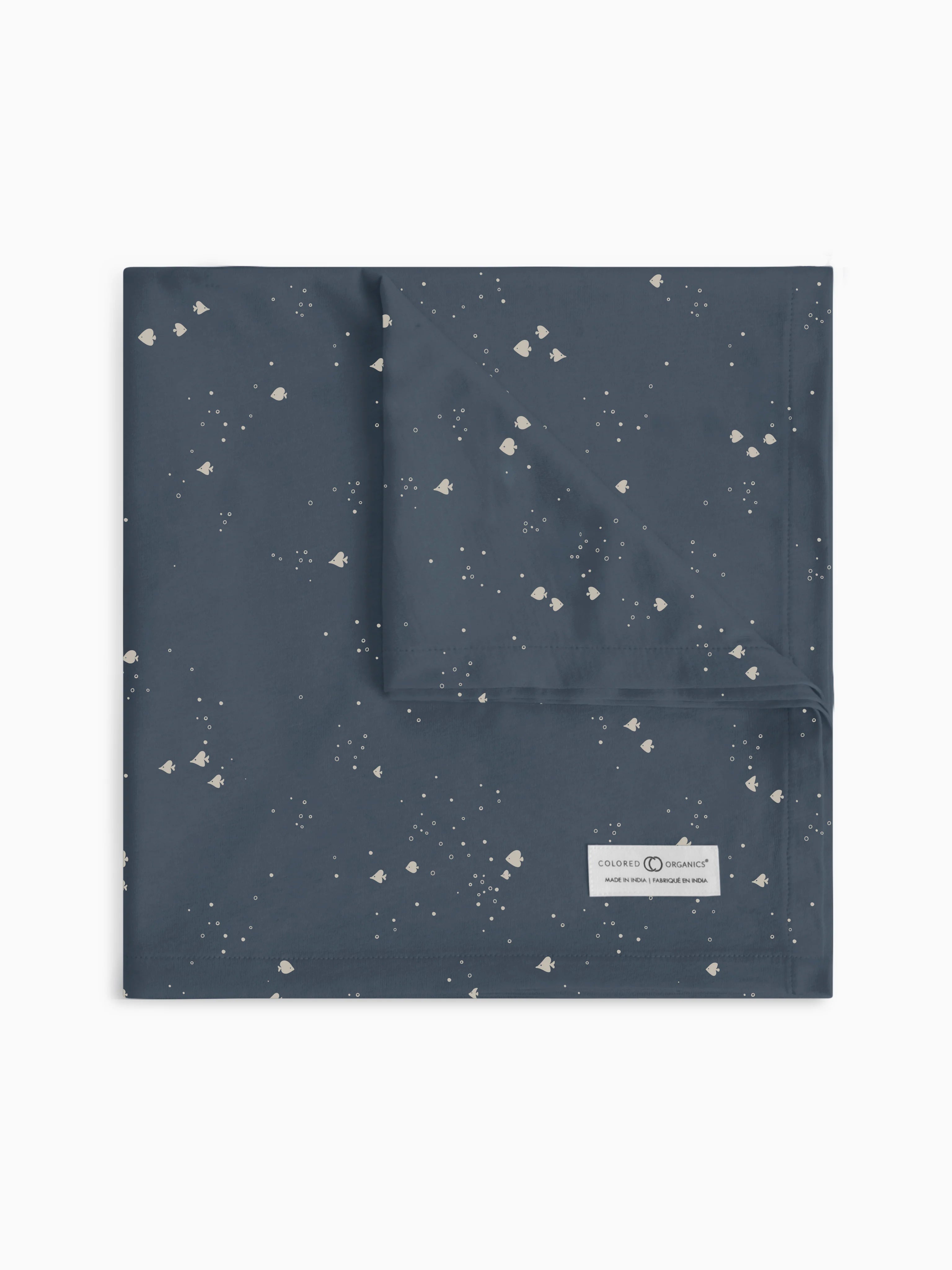 Colored Organics swaddle blanket in 'School of Fish - Harbor' design displayed flat, showcasing an array of abstract fish patterns on a navy blue background