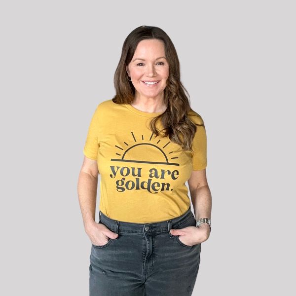 Woman wearing a mustard yellow t-shirt with the positive message 'you are golden' and a minimalist sun design.